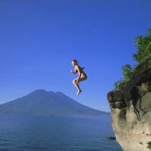 Girl jumps from cliff-side into lake.