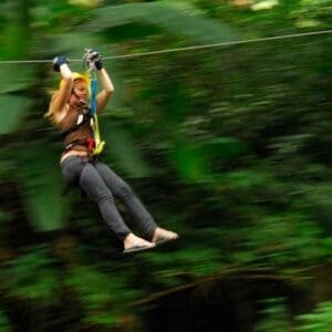 Girl whizzes down zipline cable surrounded by trees.