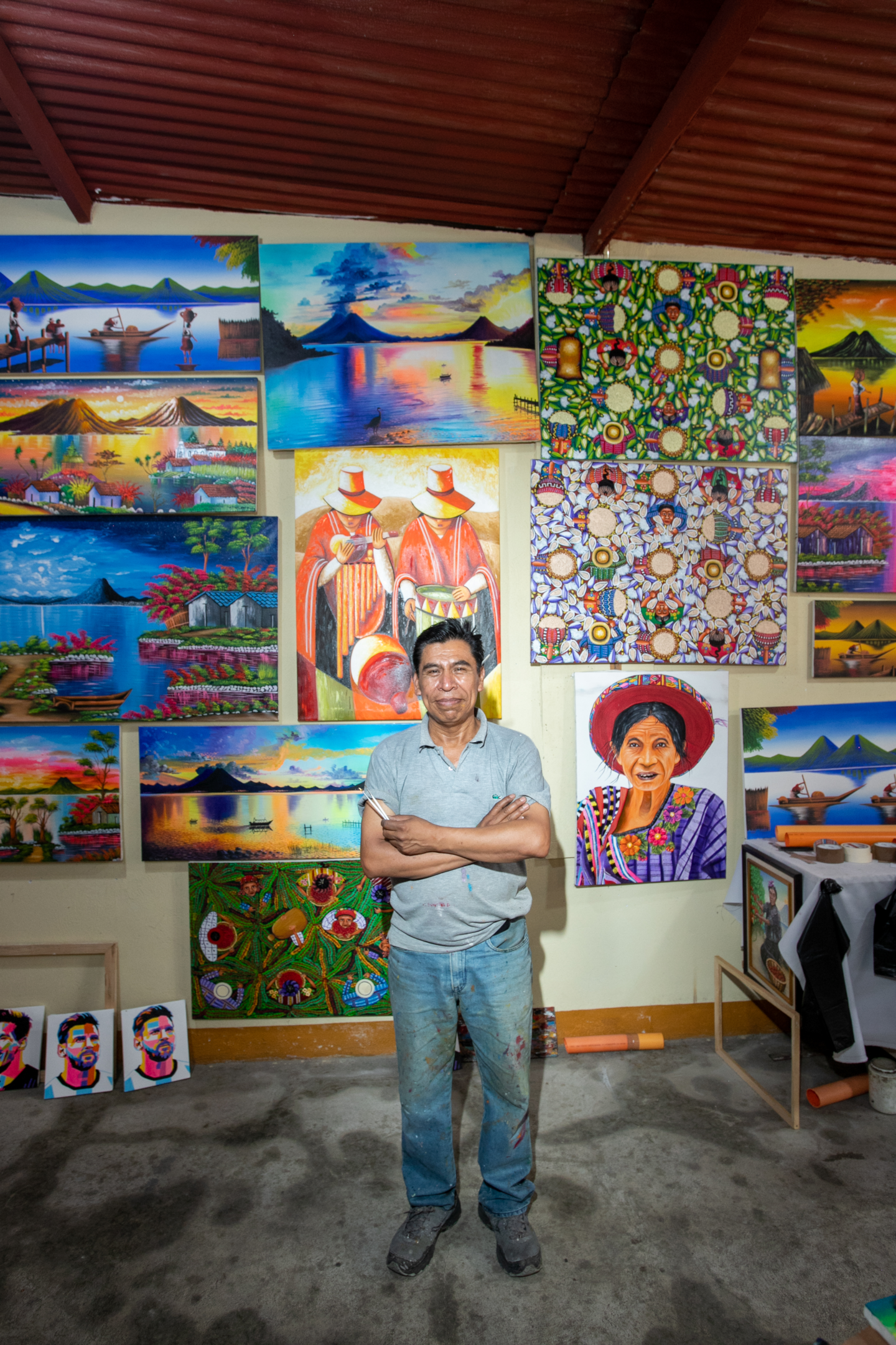 A Tz'utujil artist standing in front of a wall of oil paintings