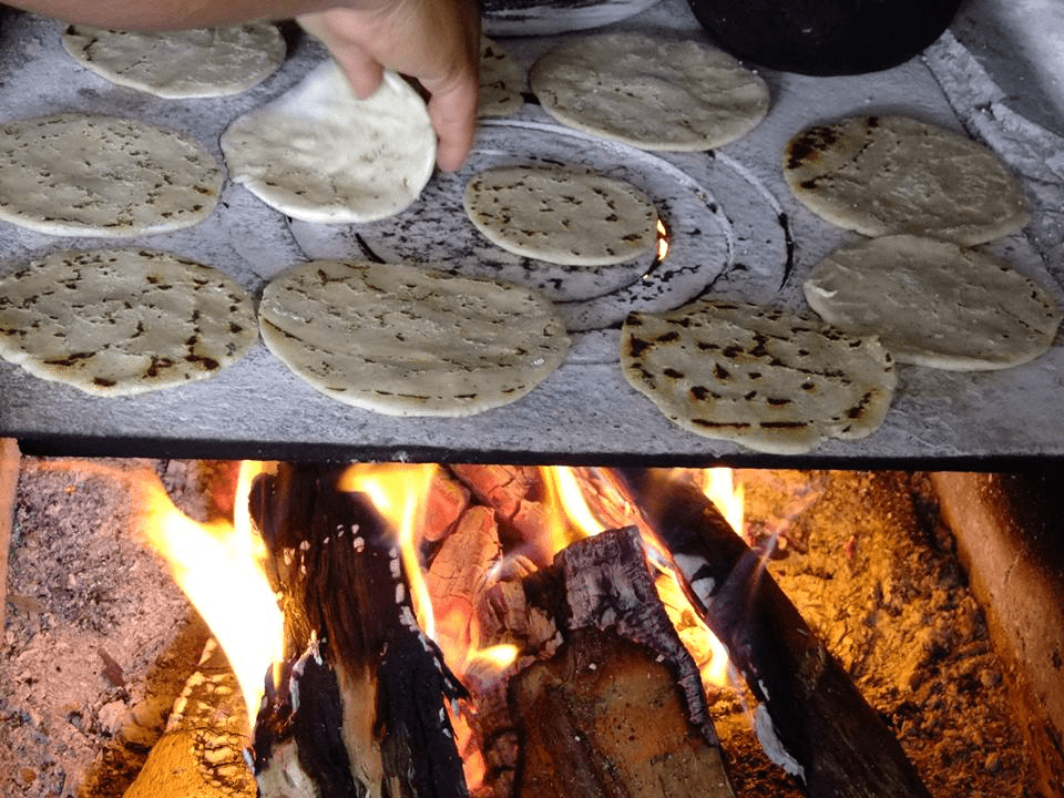 Flat cirles of tortilla dough cook on a wood fire.
