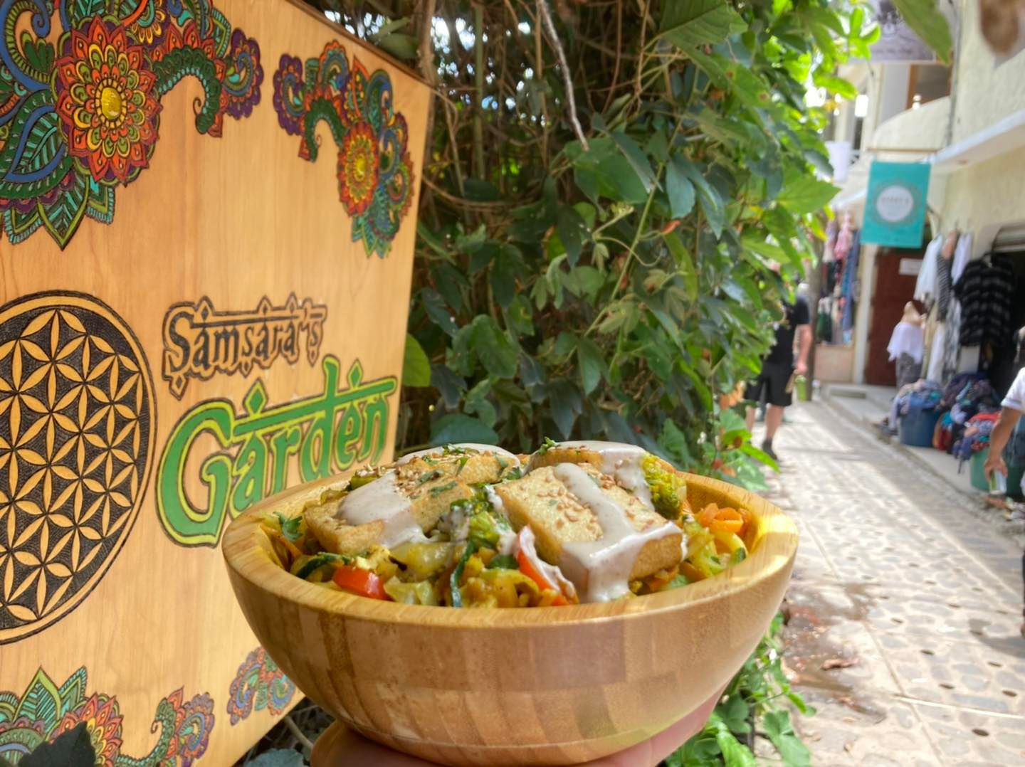 Tofu Buddha bowl held in front of the welcome sign at Samsara's Garden.