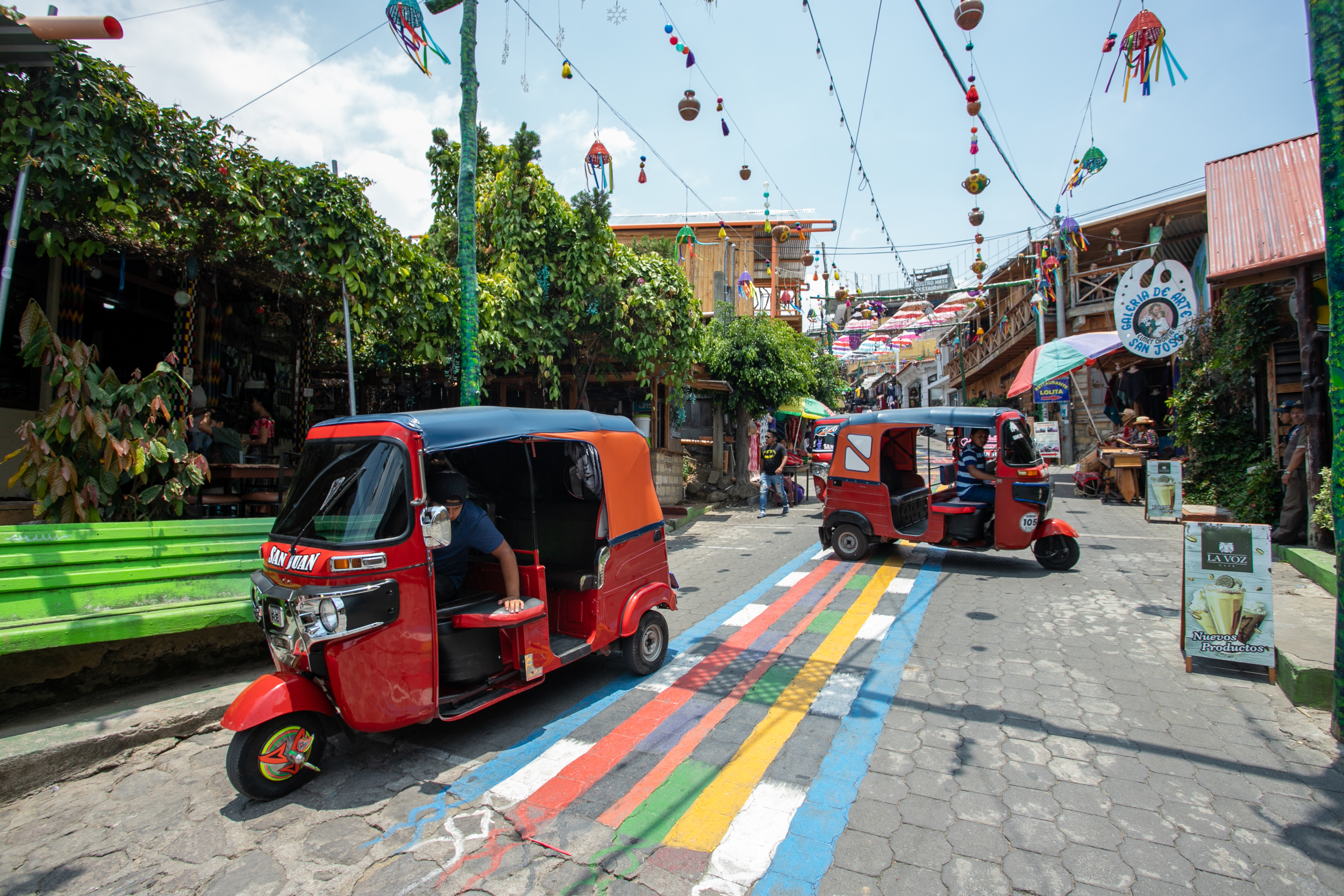 Red tuktuk's pass through a street where the floor is painted in bright colours.  