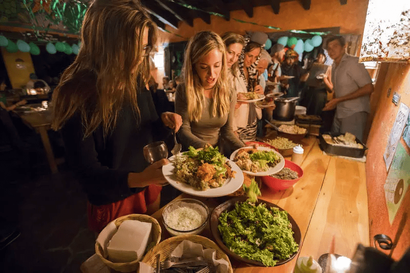 Travellers fill their plates with food in a candle-lit room.