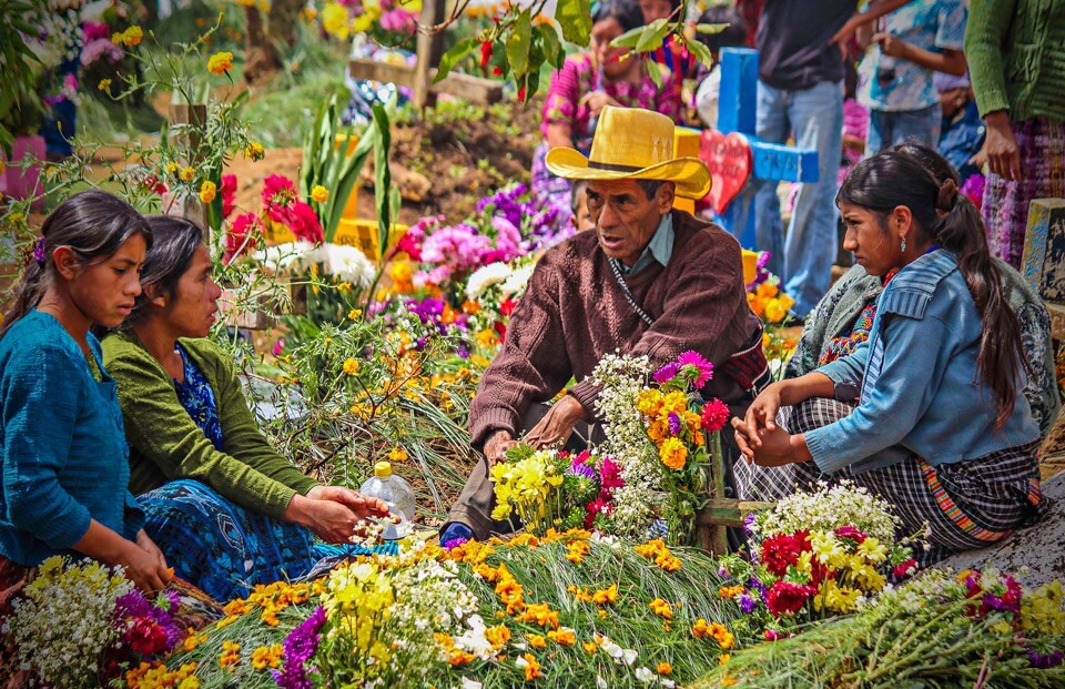 Old man wearing cowboy hat leans over a market stall full with flowers .
