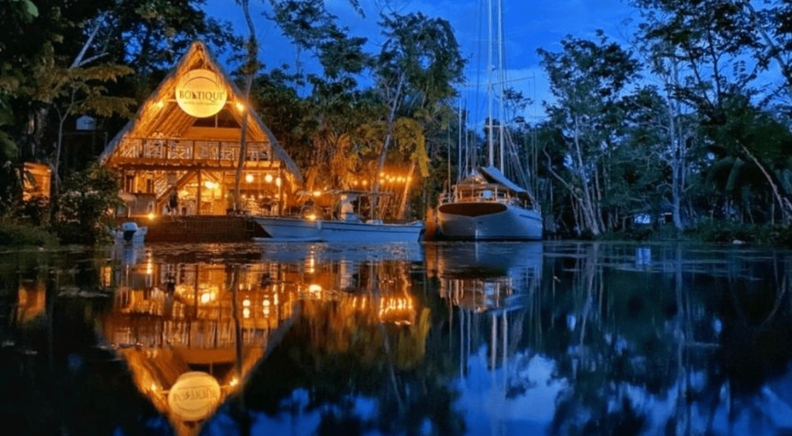 The facade of the jungle lodge Boatique Hotel and Marina at night and next to it, a yacht.