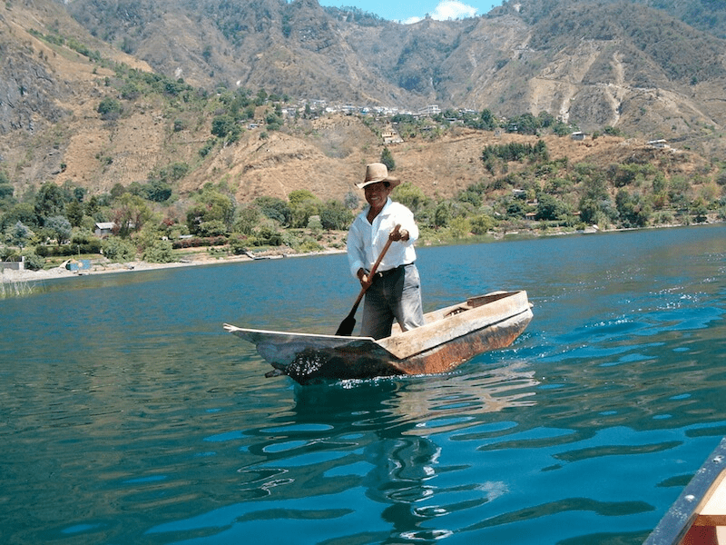 Local fisherman in dug out canoe paddles the lake's edge searching for fish.