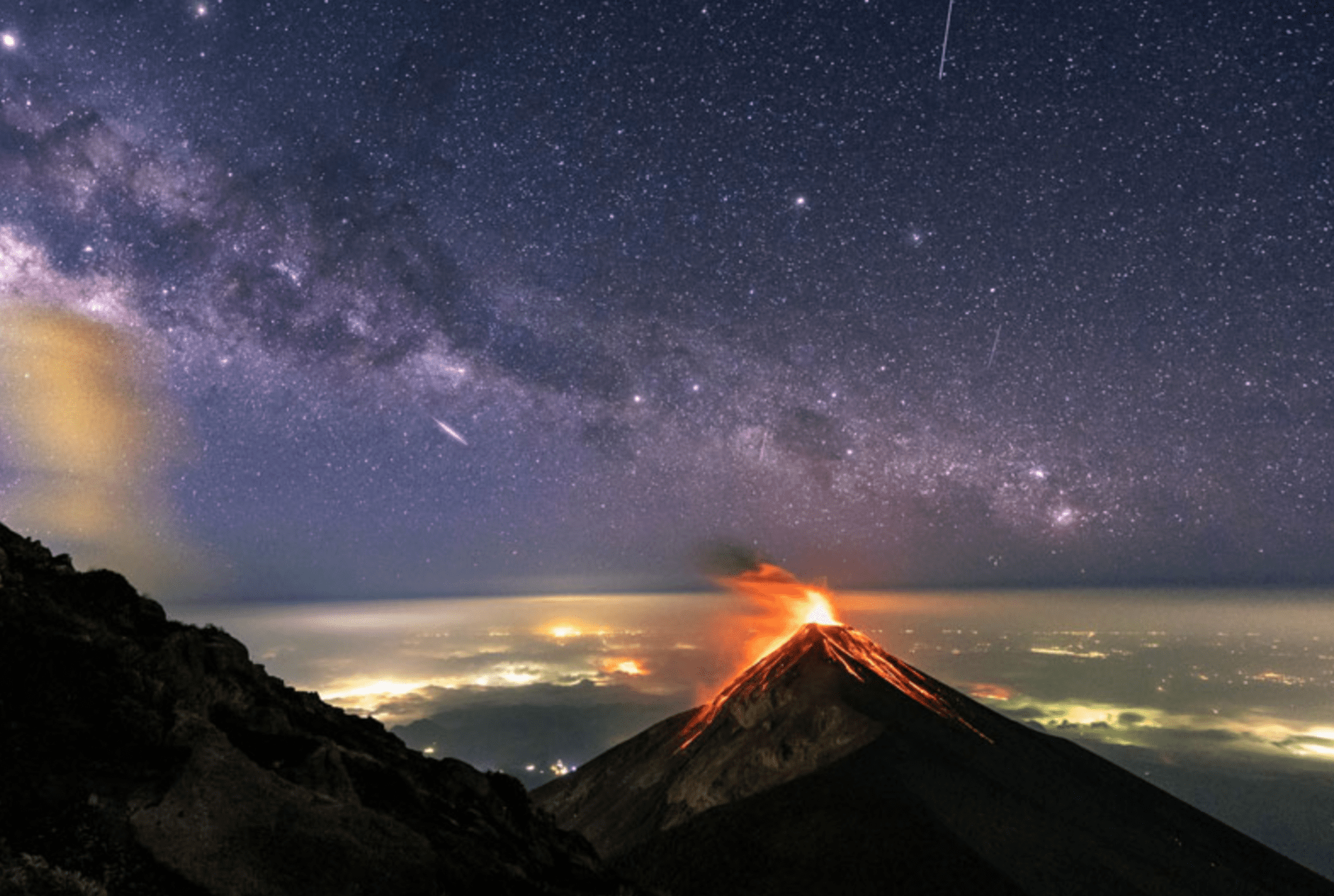 Night view of Fuego volcano with city lights in the background.